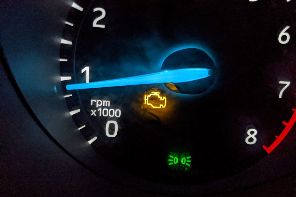 Voyant 'Check Engine' allumé en jaune sur le compteur de régime d'un tableau de bord de voiture, indiquant un problème mécanique.