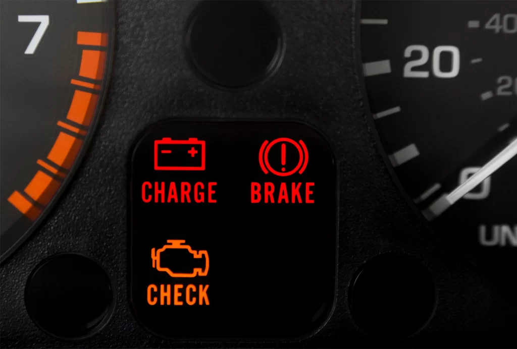 Voyants de batterie, frein de stationnement et check engine allumés sur un tableau de bord de voiture.