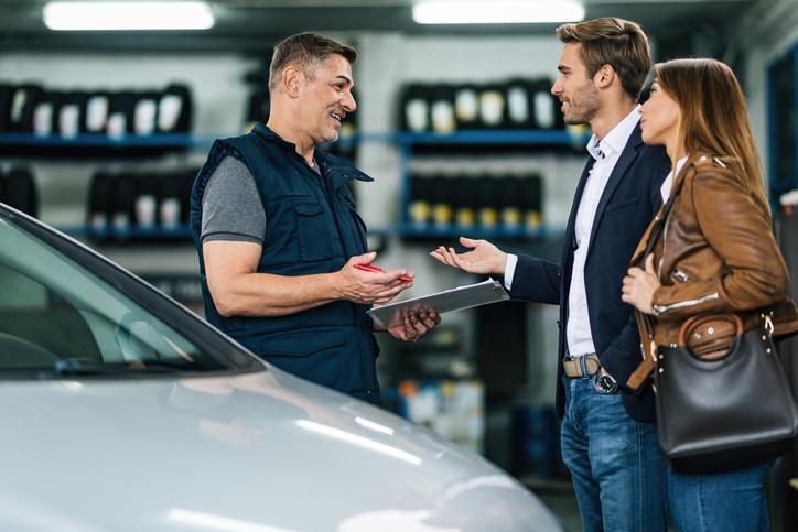 Étudiant en formation mécanique automobile dans un atelier de réparation qui parle à un client