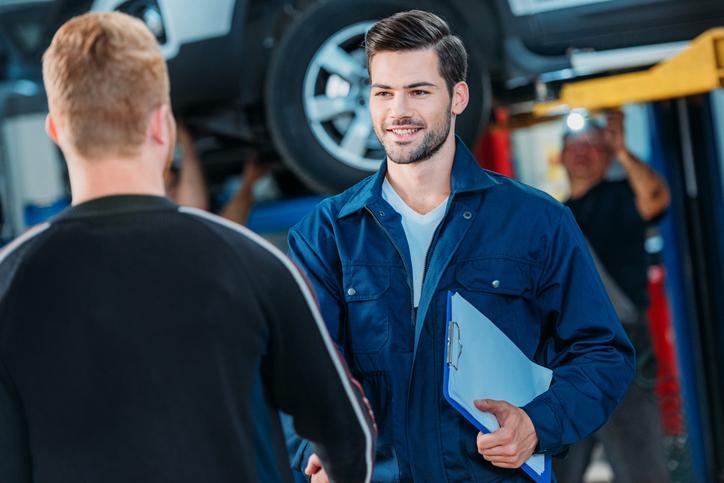 Étudiant en formation mécanique automobile dans un atelier de réparation qui parle à un client