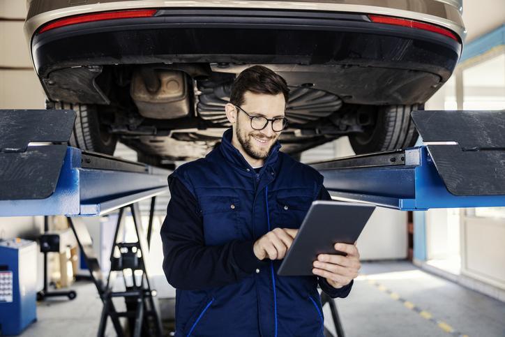 Étudiant en formation mécanique automobile qui effectue un diagnostic avec une tablette numérique.