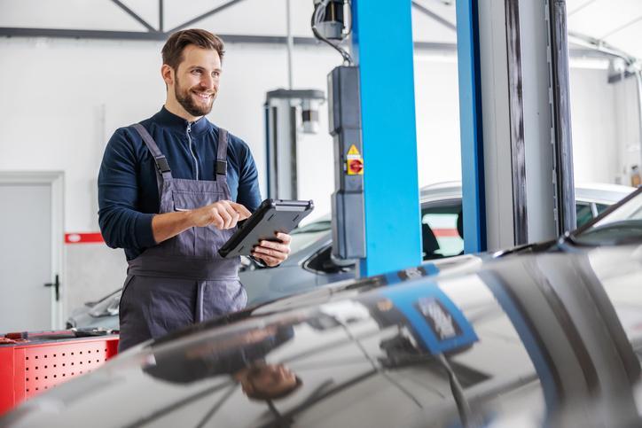 Étudiant en école mécanique auto qui travaille dans un atelier auto avec un outil d’inspection numérique.