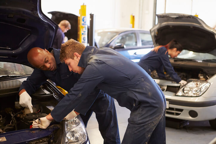 An auto mechanic training student working with an instructor at a shop