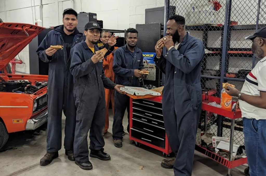 Groupe d’étudiants dans un garage, illustrant un apprentissage adapté à l’industrie automobile.