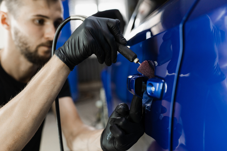 Préparateur esthétique automobile réalisant un polissage sur un véhicule de luxe.