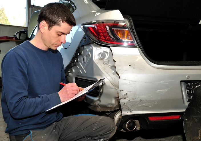 Un estimateur expert en dommages automobiles inspectant un véhicule accidenté.